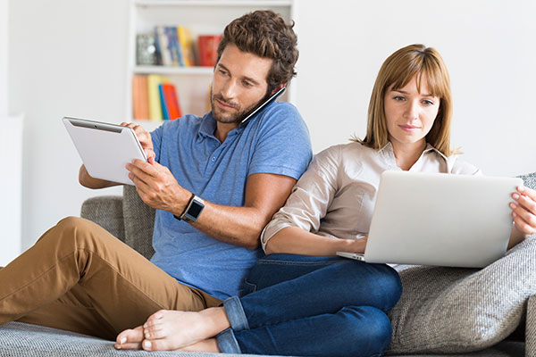 couple sitting on couch with their phones and laptop